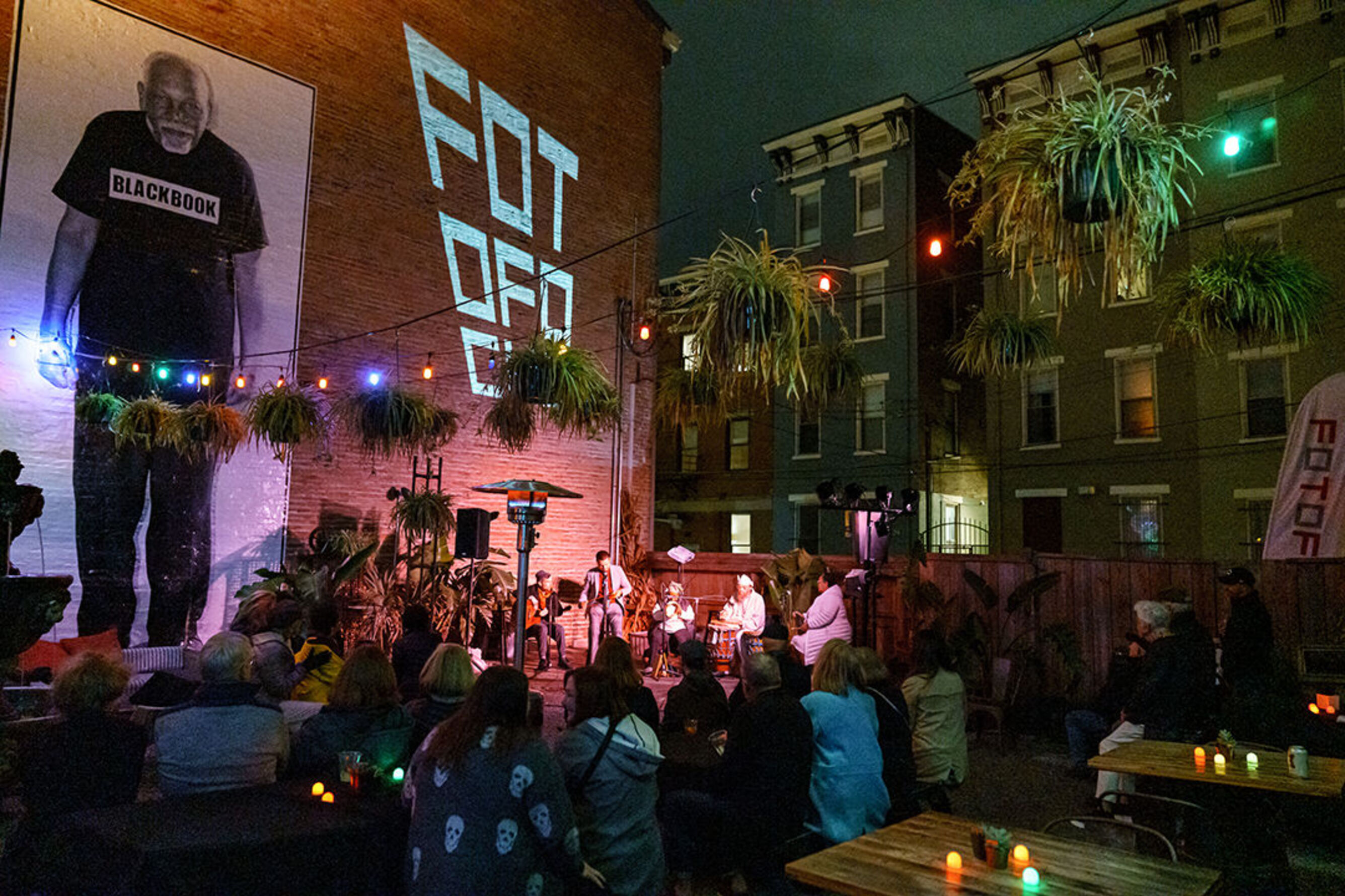 Musicians play together on a stage in the outdoor courtyard of a bar.