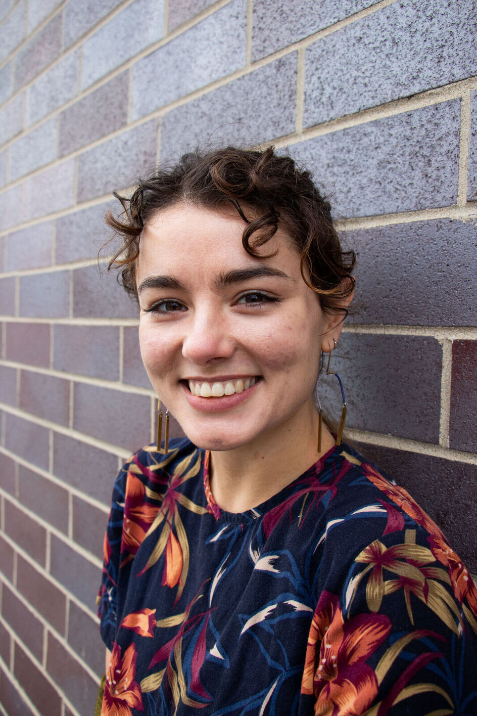 smiling woman with curly brown hair standing against brick wall