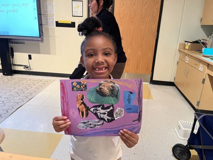 A student holds up her art collage of animals and colors inspired by poetry.