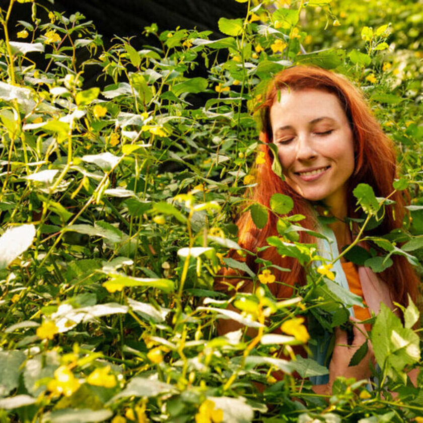 Kateri smiles with her eyes closed in a tall bush with warm sunlight.