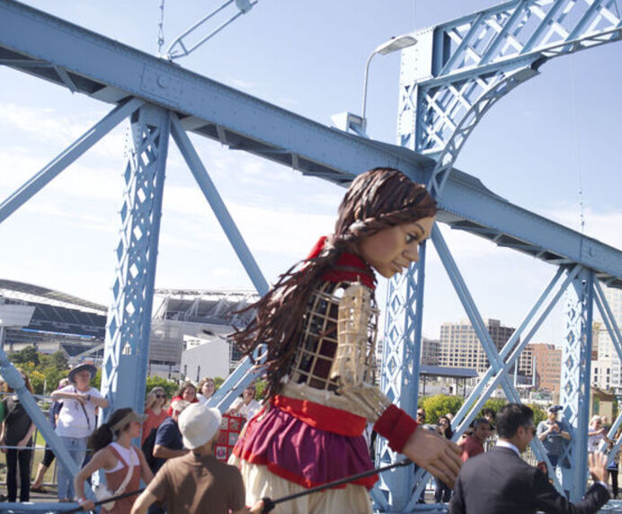 A 12-foot tall puppet crosses a bridge, holding hands with the mayor.