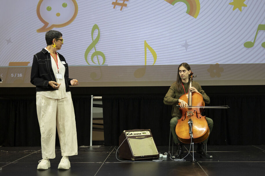 Stacy stands onstage with Bryce playing cello.